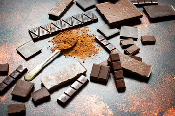 Assortment of different types of chocolate and cocoa powder on a dark background. Close-up. Space for text