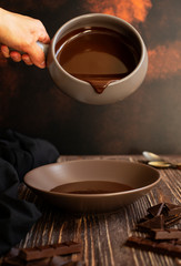 Delicious Chocolate ganache is poured from one plate to another. Hot chocolate. Dark rustic vintage background. Vertical. Close-up. Space for text