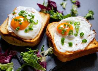 Sandwich with ham, cheese and egg. A traditional French croque-madame sandwich served with lettuce leaves on a black plate. Popular French cafe meal. Black background. Close-up