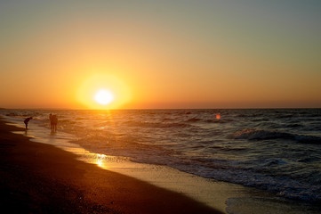 Sea Golden sunset. Waves run on the sandy shore. Silhouettes of people walking along the shore.