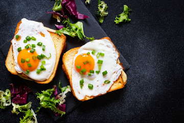 Sandwich with ham, cheese and egg. A traditional French croque-madame sandwich served with lettuce leaves on a black plate. Popular French cafe meal. Black background. Top view. Space for text