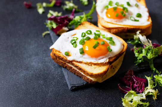 Sandwich with ham, cheese and egg. A traditional French croque-madame sandwich served with lettuce leaves on a black plate. Popular French cafe meal. Black background. Close-up