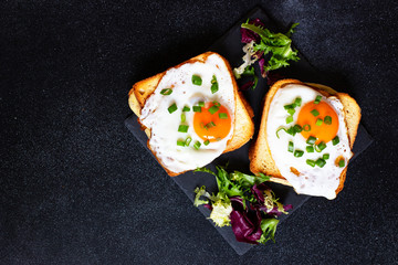 Sandwich with ham, cheese and egg. A traditional French croque-madame sandwich served with lettuce leaves on a black plate. Popular French cafe meal. Black background. Top view. Space for text