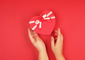 two hands hold a paper closed red box in the shape of a heart