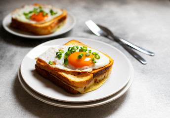 Sandwich with ham, cheese and egg. A traditional French croque-madame sandwich served on a white plate. Popular French cafe meal. Gray background. Close-up. Space for text