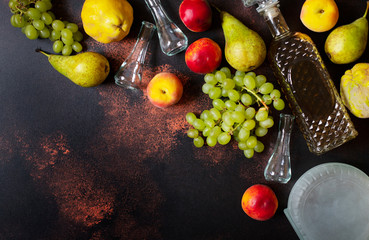 Rakia or Rakija the traditional balkan fruit brandy. The fruits of which produce Rakia. Fruits, bottles and glasses for alcohol. Top view. Dark vintage background. Space for text