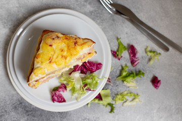Sandwich with ham, cheese and bechamel sauce. A traditional french croque-monsieur sandwich served with lettuce leaves on a white plate. Gray background. Top view. Space for text