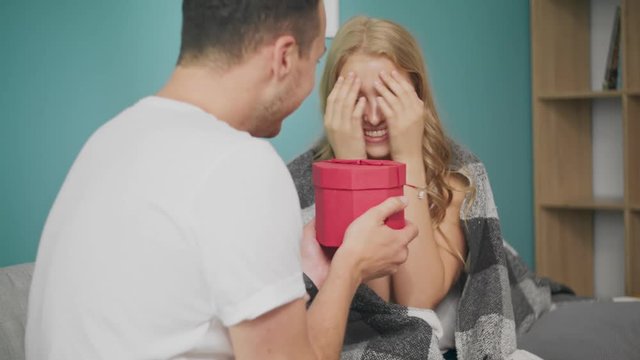 Young man gives a gift to a happy girlfriend in the morning in the living room