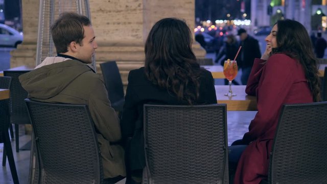 Man flirting with a friend while kissing his girlfriend sitting at caf&egrave;