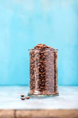 Coffee beans in glass jar on blue background copy space