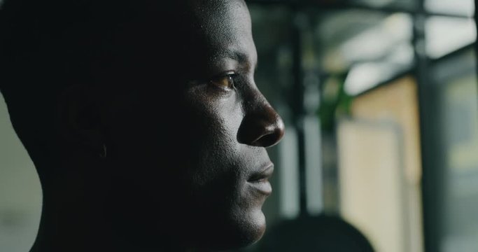 Cinematic close up shot of a professional young muscular african man is taking a breath after a practicing shadow boxing work out in a gym with ring.