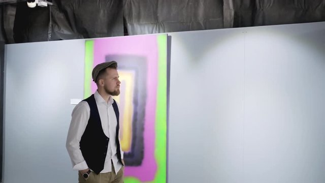 Male art lover is strolling in hall of art gallery and viewing pictures