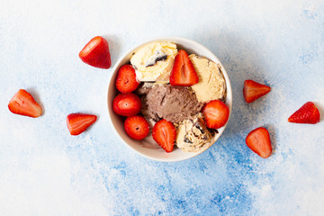 Chocolate and vanilla ice cream in a white bowl with fresh strawberries. Light blue background. Top view. Copy space