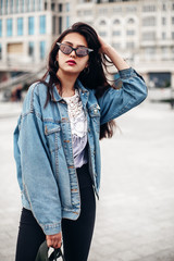 Interested glamorous woman in oversized denim jacket makes selfi. Gorgeous brunette girl posing on city background