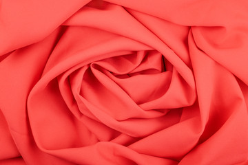 Texture of the red coral matt fabric with folds. Closeup of rippled red silk fabric in rose form