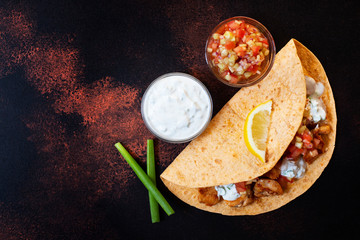 Traditional Mexican fajitas with chicken and vegetables, served in tortilla with white and red sauce, lemon and fresh green onions. Top view. dark background. Copy space