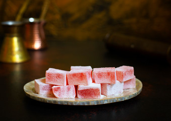 Rosewater-flavored Turkish Delight or Rahat Lokum (Loukoumi, Ratluk) on a vintage plate. In the background are two copper vintage cezves and a coffee grinder. Golden background. Front view. Copy space