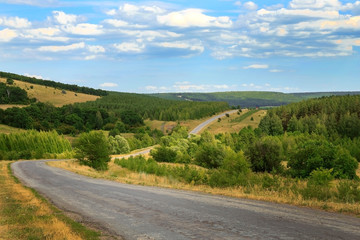 Fototapeta na wymiar Travel and tourism. Landscape, road stretching into the distance among beautiful green forests and hills on a summer day in good weather against a blue sky
