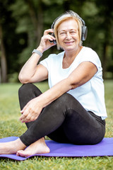 Happy senior woman listening to the music with headphones while practising yoga in the park. Concept of an active lifestyle on retirement