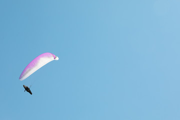 Fototapeta na wymiar Skydiver with a white-pink parachute flies across the blue sky