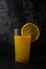 Orange juice with slice of orange on dark background.