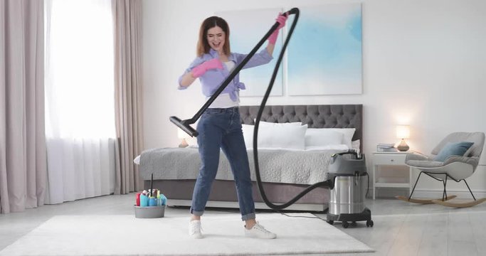 Funny woman dancing while cleaning carpet in bedroom