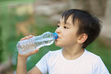 Cute asian child boy drinking clear water outdoors. Pure water