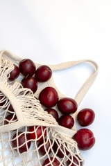 Plums in an ecological cotton reusable string bag, an alternative to plastic bags, on a white background. top view.