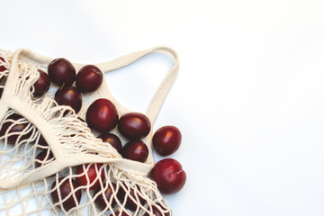 Plums in an ecological cotton reusable string bag, an alternative to plastic bags, on a white background. top view.