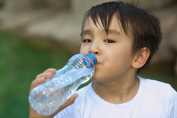 Cute asian child boy drinking clear water outdoors. Pure water