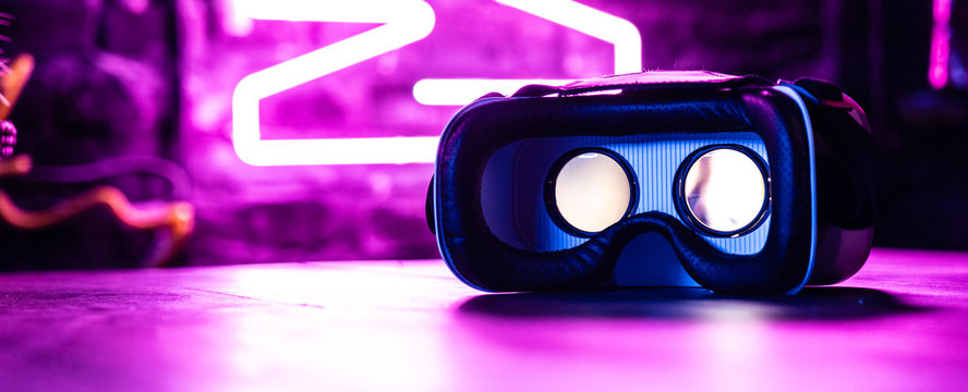 VR 3d 360 headset glasses goggles in futuristic purple neon light on table desk, virtual augmented ar reality innovative experience digital technology background concept, copy space wide photo banner
