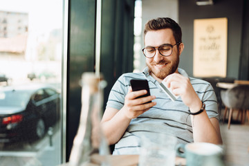Portrait of smiling man shopping online with smartphone and paying by credit card