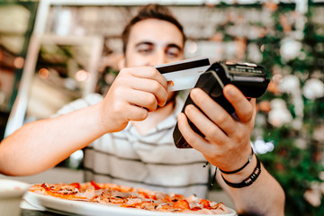 Smiling man paying at restaurant using smartphone. mobile paying technology with contactless credit card