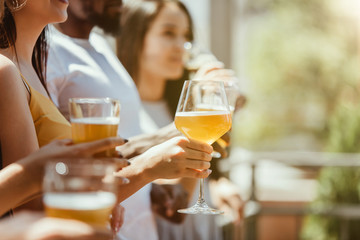 Young group of friends drinking beer, having fun, laughting and celebrating together. Women and men with beer's glasses in sunny day. Oktoberfest, friendship, togetherness, happiness, summer concept.