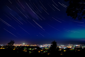 Star trails in clear night sky above the city with many lights view from mountain