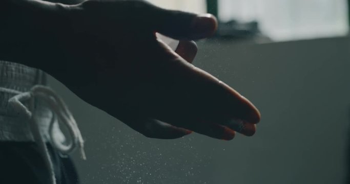 Cinematic slow motion close up shot of a professional young muscular african man is putting a talc powder to his hands before to start practicing shadow boxing work out in a ring.