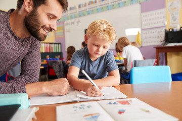 Elementary School Teacher Giving Male Pupil One To One Support In Classroom