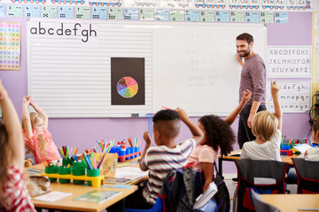 Pupils Raising Hands To Answer Question In Elementary School Maths Lesson