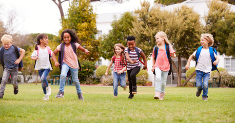 Obraz na płótnie Canvas Excited Elementary School Pupils Running Across Field At Break Time