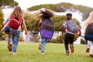 Rear View Of  Elementary School Pupils Running Across Field At Break Time