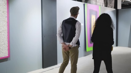 Man and woman are moving in hall of art gallery and talking about pictures