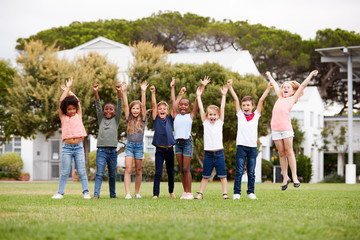 Obraz premium Group Of Excited Elementary School Pupils Standing On Playing Field At Break Time With Arms Raised
