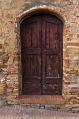 Architectural details of a weathered doors on an old brick house in a narrow winding streets at San Gimignano, Tuscany, Italy
