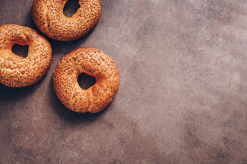 Flat lay three bagels with sesame on a dark rustic background. Top view, copy space.