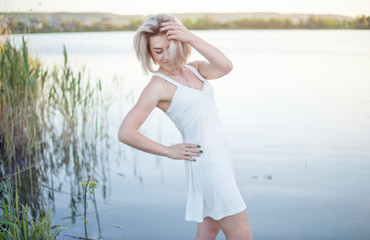 The girl in the white dress on the lake enjoys the summer.