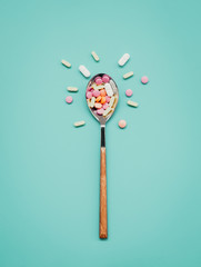 Pharmaceutical medicine tablets, tablets and yellow capsules on an iron spoon on a blue background. the concept of health. top view. minimalism