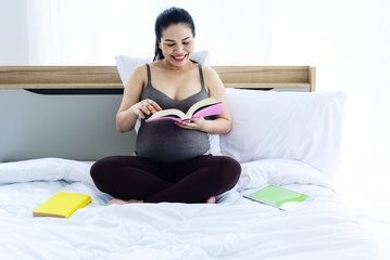 The pregnant woman sitting on bed,reading book with smile and happy feeling,blurry light around