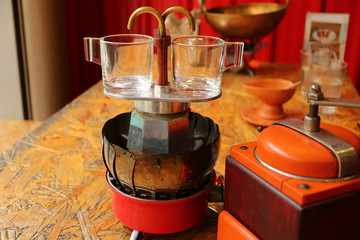 Pair of empty transparent demitasse espresso cups on the stove top mini coffee brewer with coffee grinder in foreground