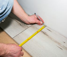 Fototapeta na wymiar Worker making laminate flooring in apartment. Measure tape and pencil in hands. Maintenance repair renovation. Wooden parquet planks indoors.