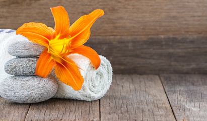 Obraz na płótnie Canvas Spa setting with orange lily flower on towel and stones against wooden background